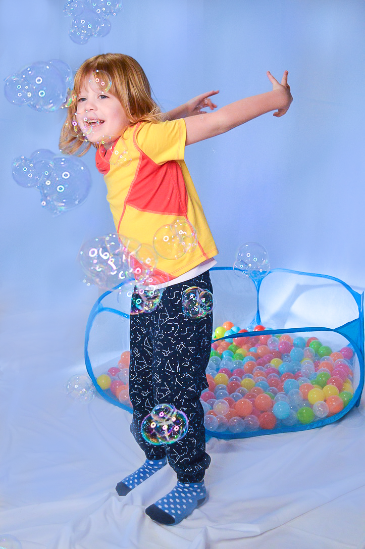 Autistic child in sensory room with calming bubbles and fun ball pit for sensory regulation.